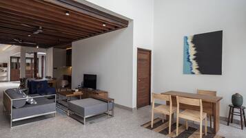 A modern living room with a sofa, a TV, a wooden dining table, and a painting on the wall.