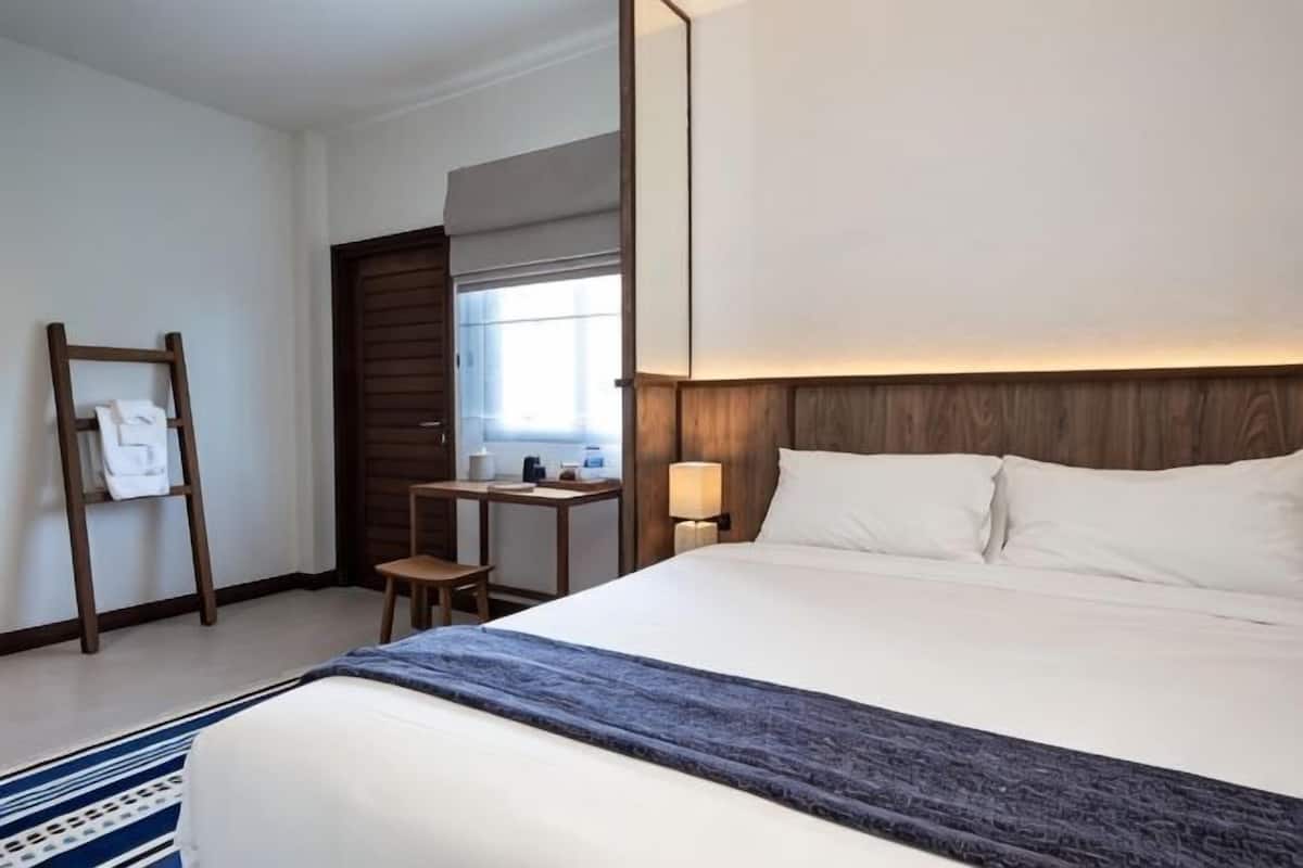 Ein Hotelzimmer mit einem großen Bett, einem Schreibtisch, einem Sessel, einem Nachttisch und einem Fenster.