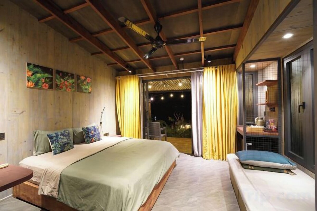A bedroom with a bed, bedside table, and a view of the outdoors.