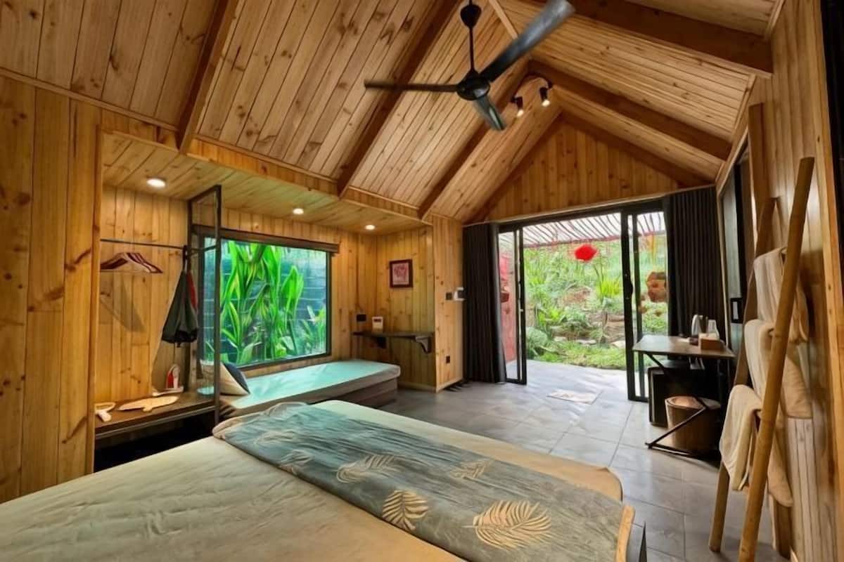 A wooden interior with a bed, a desk, and a view of greenery outside.