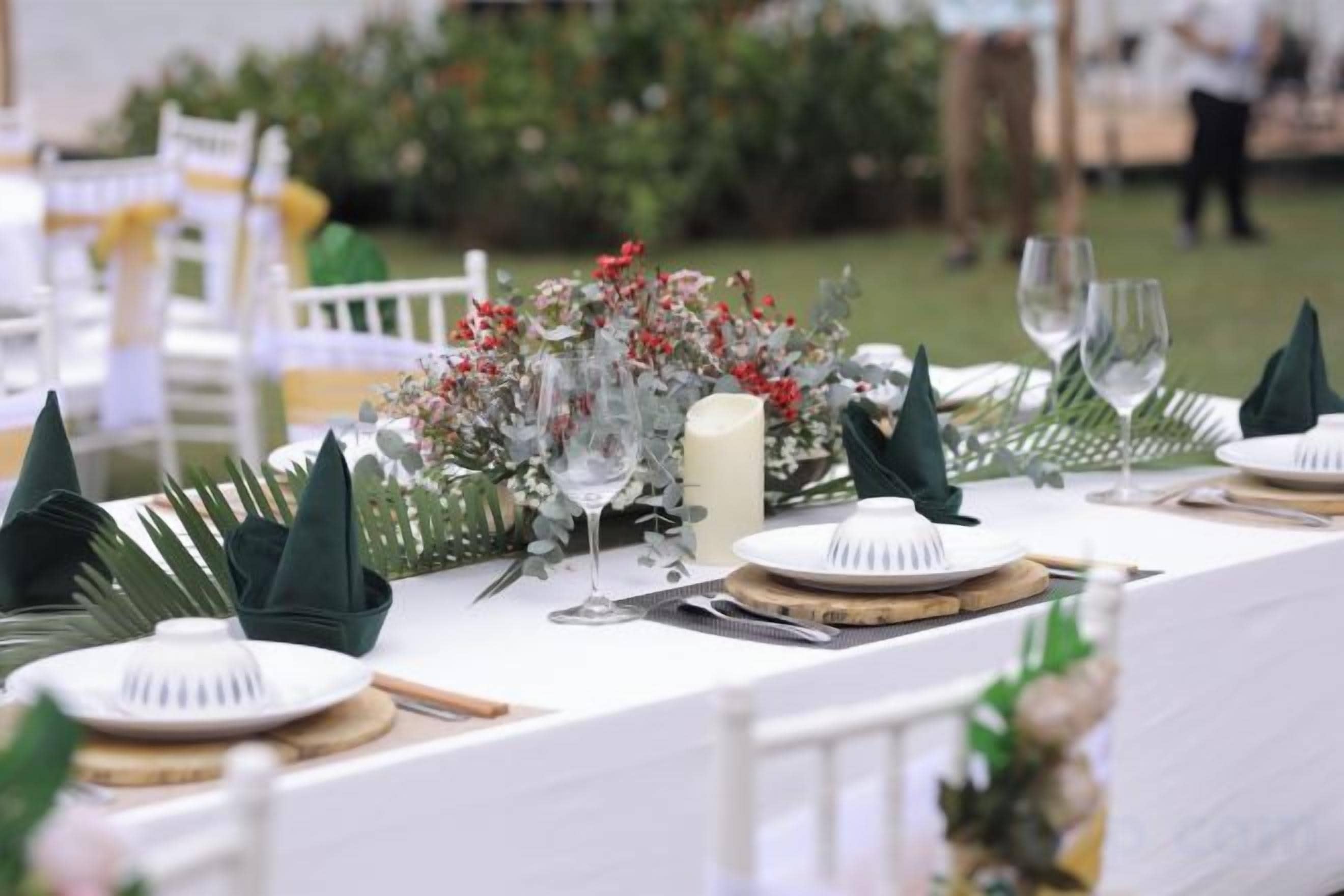 A table set with white plates, cutlery, and a candle, with a floral centerpiece and green napkins.