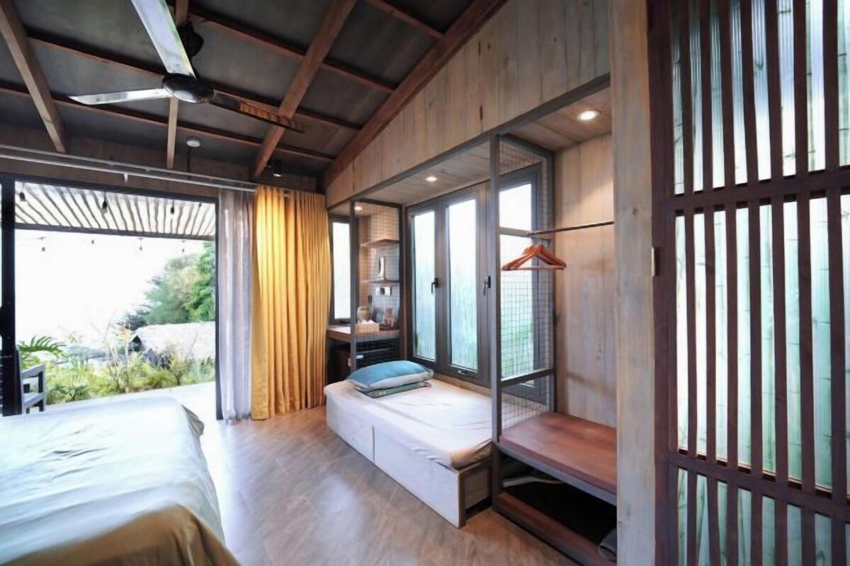 A bedroom with a bed, a bench, a hanging rack, and a view of greenery.