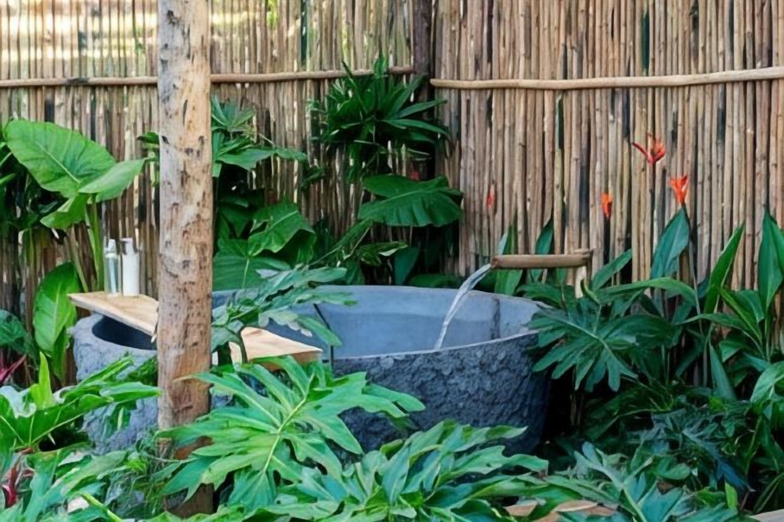 Uma cerca de bambu, um elemento de água e vegetação exuberante.