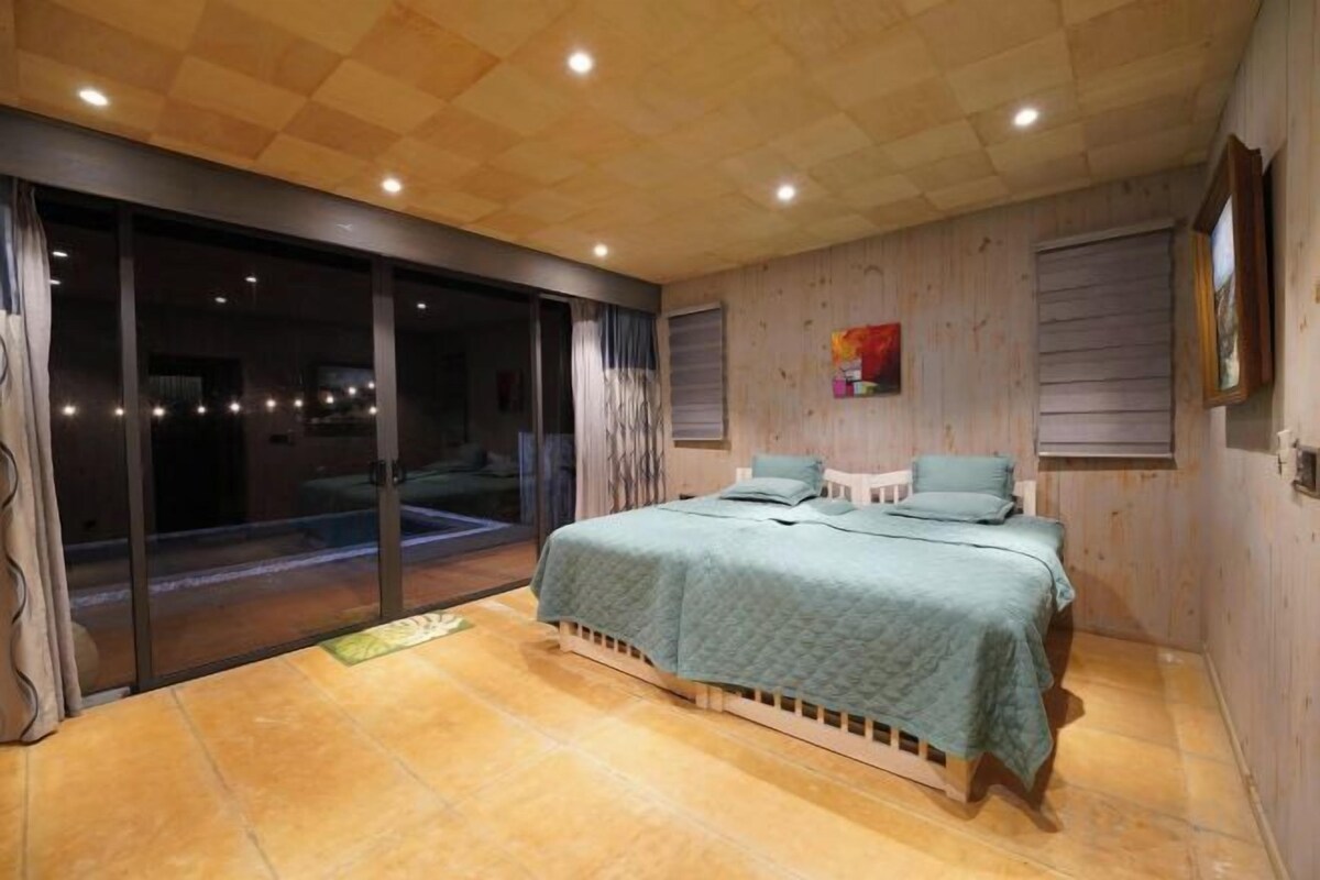 A bedroom with a bed, a sliding glass door leading to a balcony, and wooden paneling on the walls.