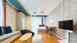 A modern hotel room with a sofa, a small table, a TV, and a bed.