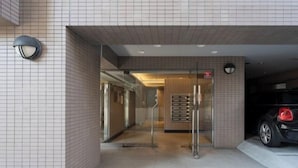 A modern building entrance with a tiled facade, a glass door, and a car parked inside.