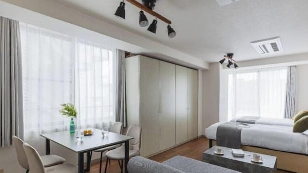 A modern hotel room with a dining table, two beds, a sofa, and a small coffee table.