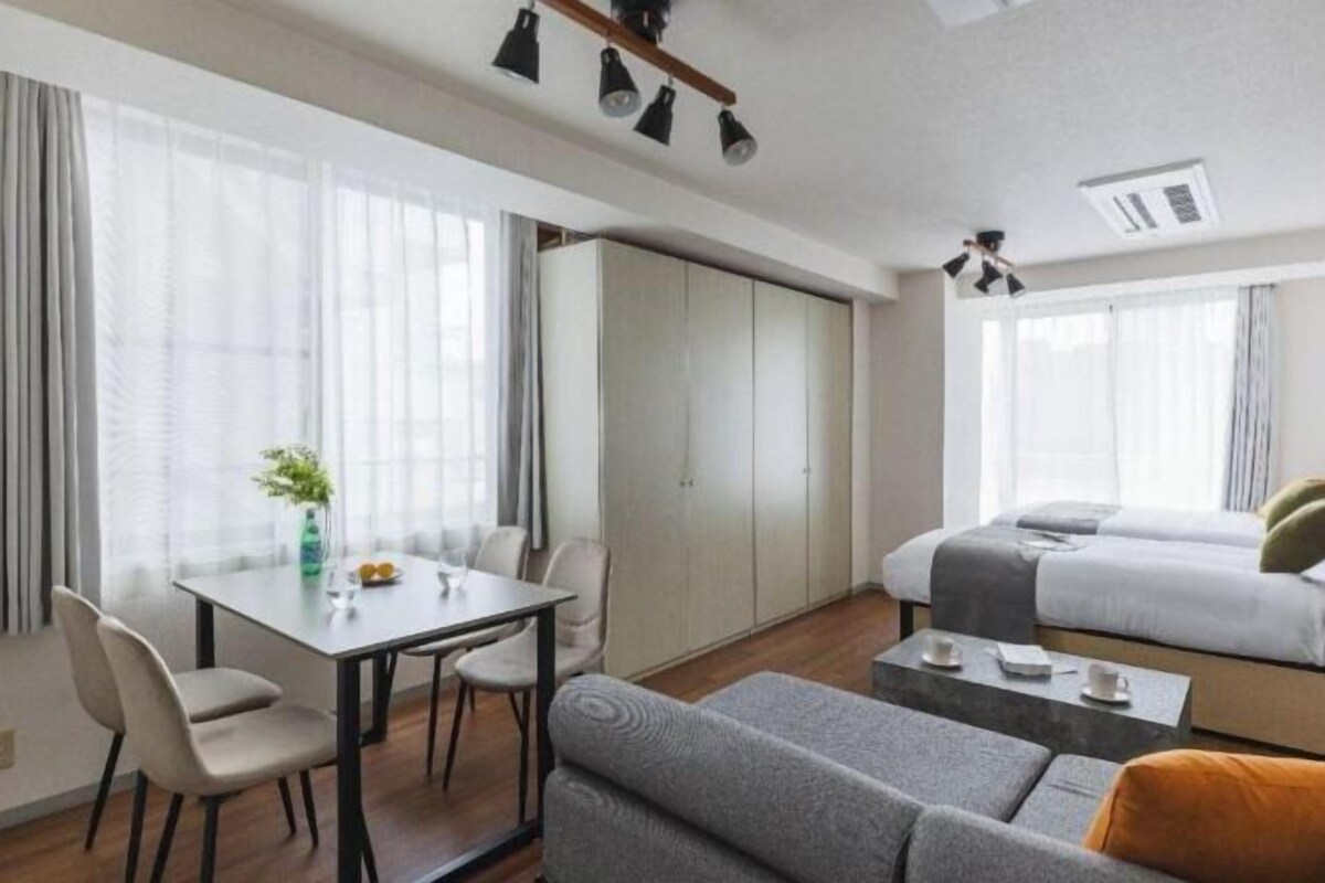 A modern hotel room with a dining table, two beds, a sofa, and a small coffee table.