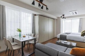 A modern hotel room with a dining table, two beds, a sofa, and a small coffee table.