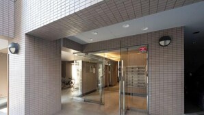 A modern building entrance with a tiled facade, glass doors, and a visible fire alarm.