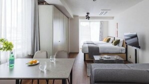 A modern hotel room with a dining area, a sofa, a bed, and a TV.