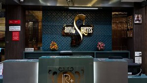 Un mostrador de recepción de hotel con un cartel que dice 'ROYAL SUITES' y un logotipo con 'R+'. 