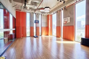 An indoor basketball court with a wooden floor, large windows, and a basketball hoop.