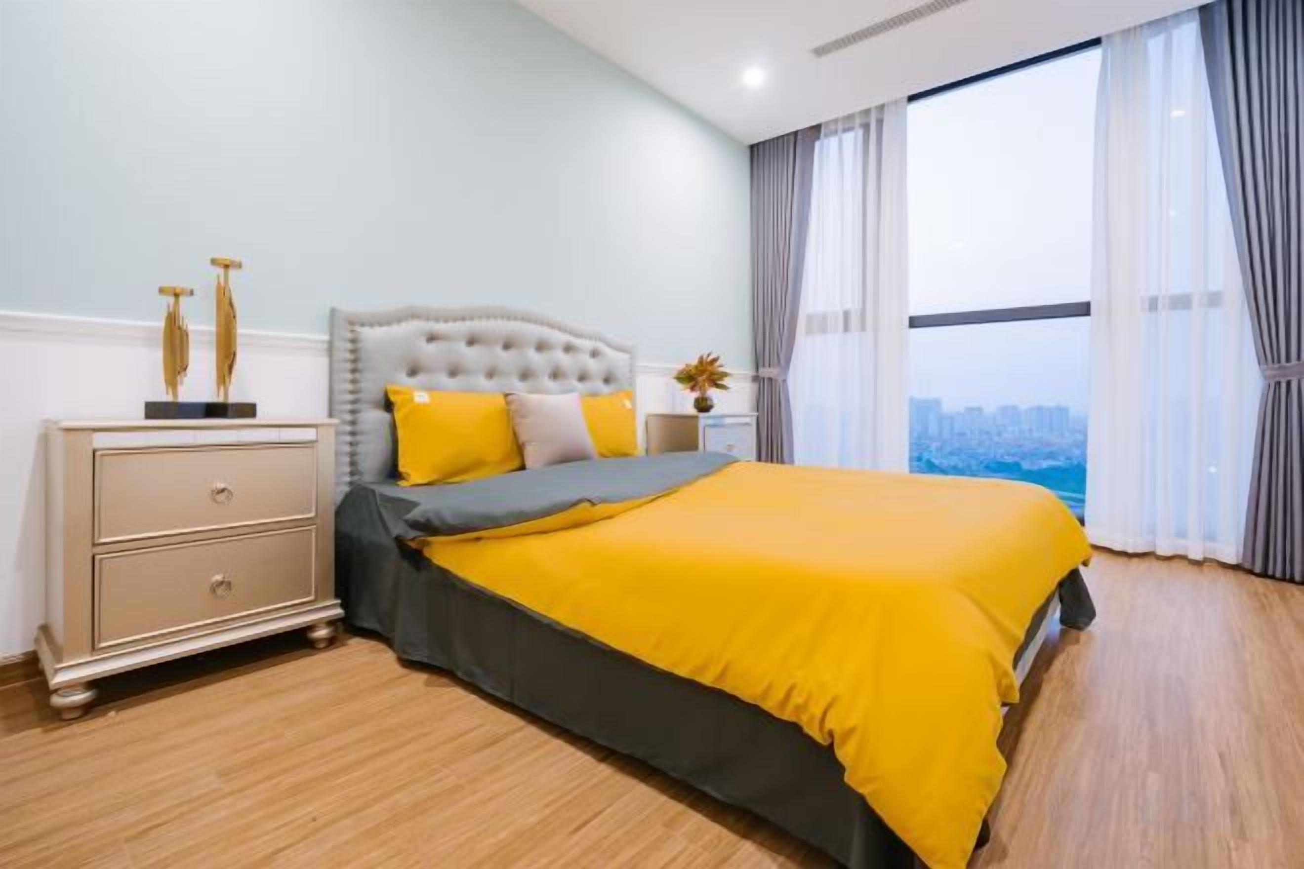 A bedroom with a bed, a nightstand, a window with curtains, and a view of a cityscape.