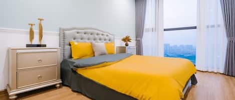 A bedroom with a bed, a nightstand, a window with curtains, and a view of a cityscape.