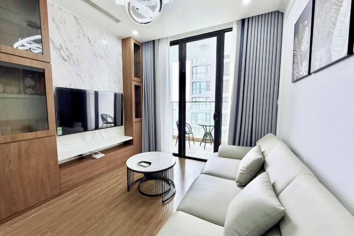 Ein modernes Wohnzimmer mit einer Couch, einem Fernseher, einem kleinen runden Tisch und einer Schiebetür zu einem Außenbereich.