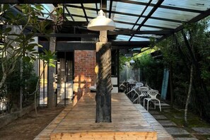 A covered outdoor area with a wooden floor, a central column, and a hanging light fixture. - The Seven Gardens Resort & Spa (Badang)