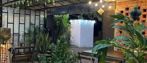 Un espace extérieur aménagé en patio, avec des sièges, des plantes en pot et des guirlandes lumineuses.