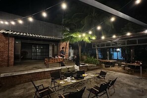 An outdoor dining area with tables and chairs, a brick building, and string lights. - The Seven Gardens Resort & Spa (Badang)
