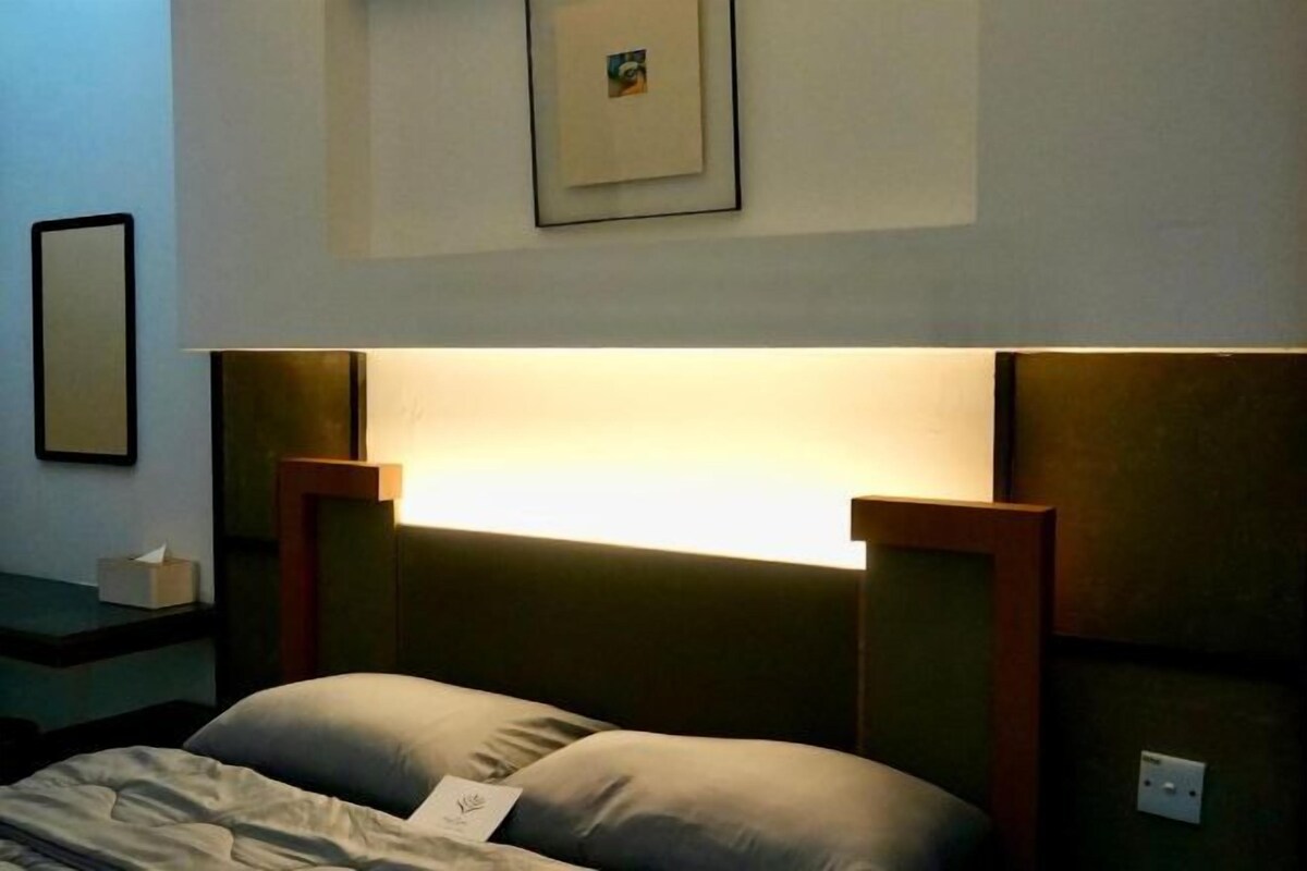 A hotel room with a bed, bedside table, and a wall-mounted light fixture.