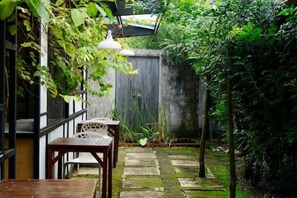 A garden patio with wooden tables and chairs, a stone pathway, and a wooden fence. - The Seven Gardens Resort & Spa (Badang)