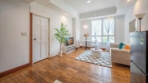 A modern living room with a wooden floor, a sofa, a TV, a dining table with chairs, and a potted plant. - The Manor 2 studio- free rooftop pool and free pick up for 5 nights (Ho Chi Minh City)
