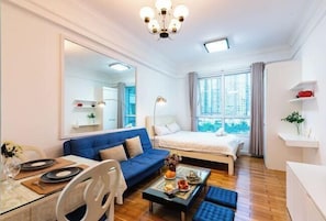 A modern hotel room with a large bed, a sofa, a dining table with plates, and a coffee table with fruits. - The Manor 2 studio- free rooftop pool and free pick up for 5 nights (Ho Chi Minh City)