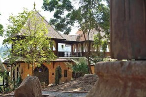 A traditional brick building with a balcony, surrounded by trees and a gravel path. - Chateau Orientale (Luang Prabang)