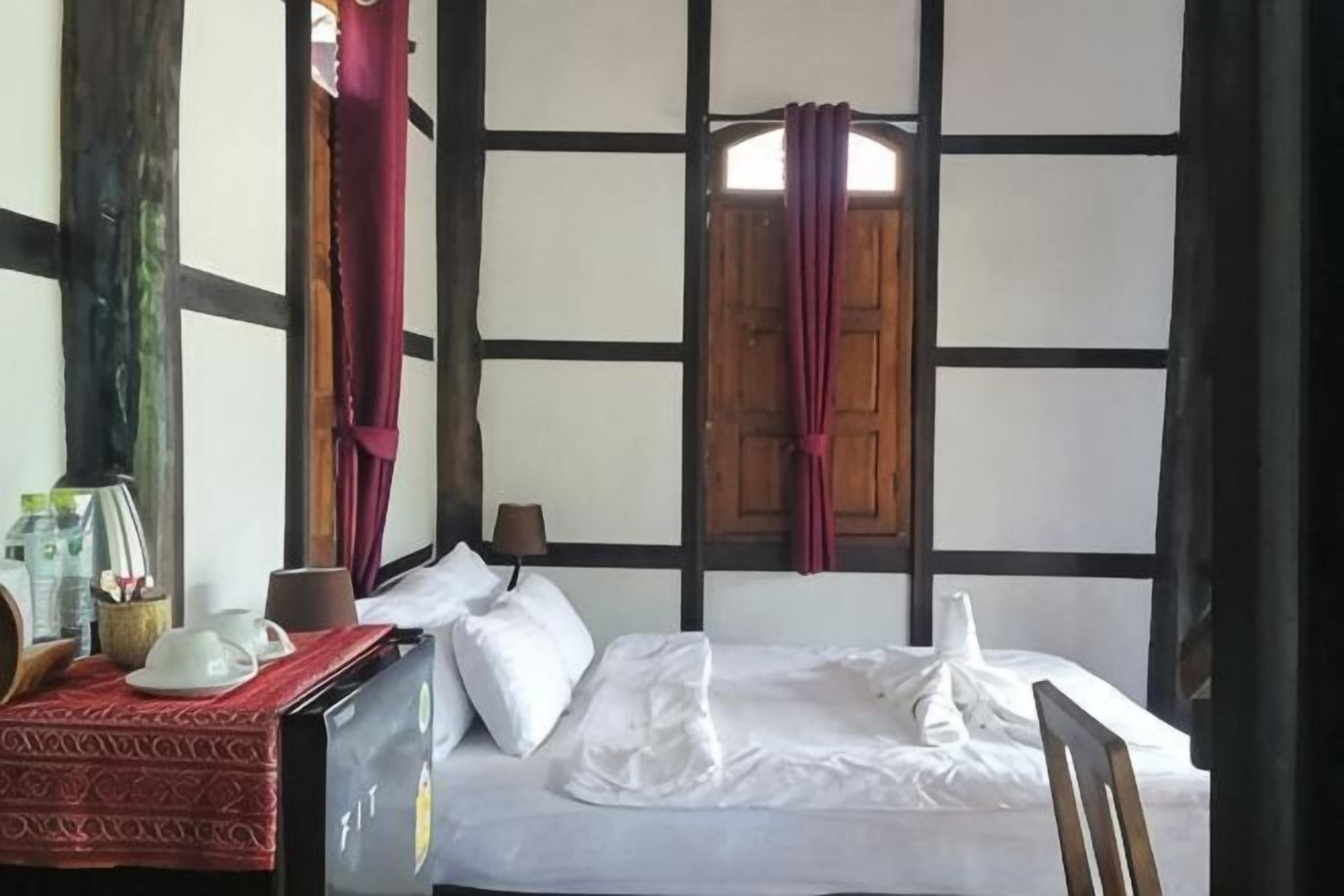 Una habitación con una cama, una mesa con mantel rojo, una ventana con contraventanas de madera y una pared con vigas a la vista.