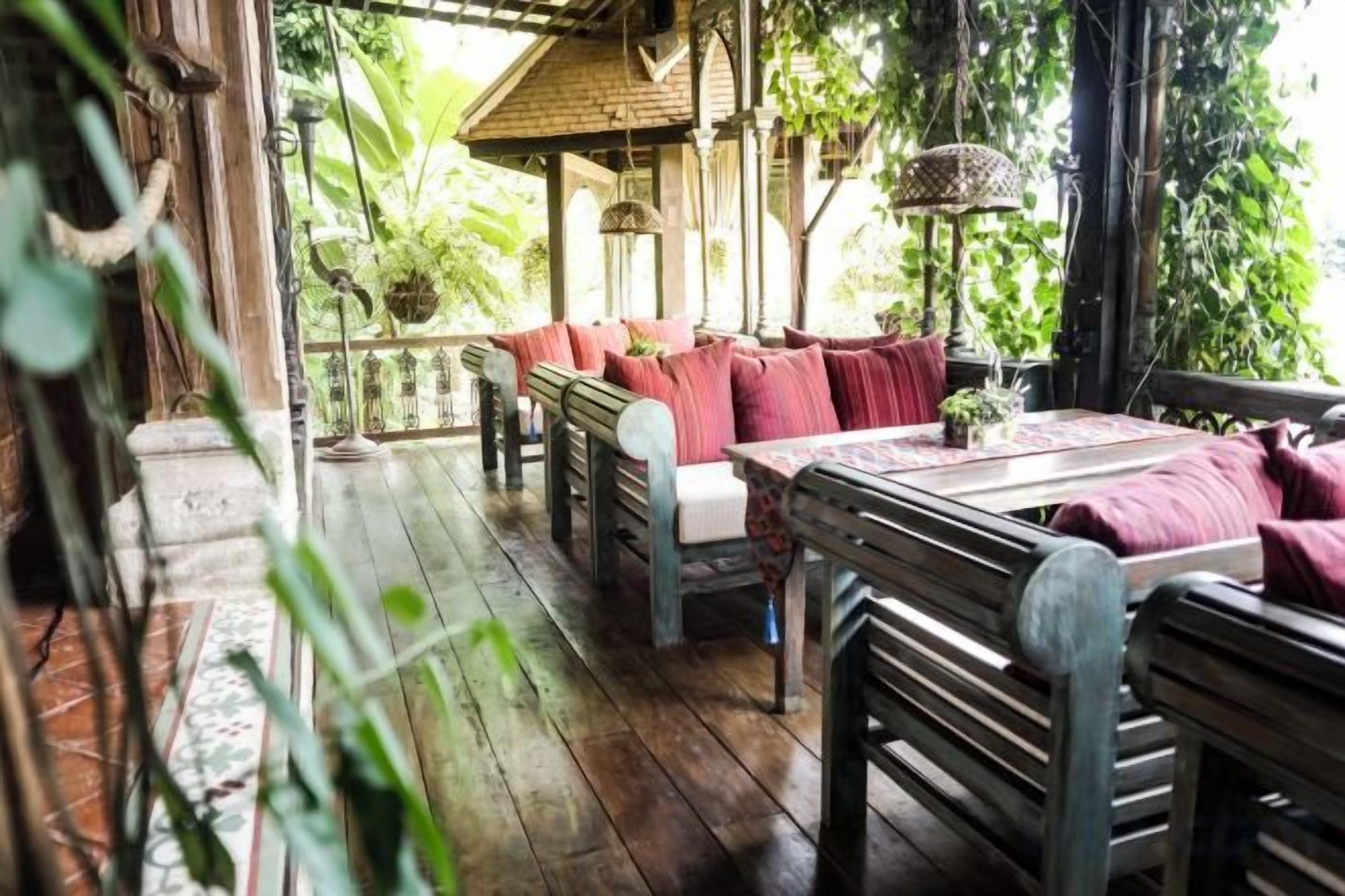 A wooden deck with benches and a table, surrounded by lush greenery.
