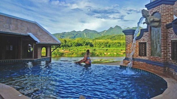 A woman sitting in a hot tub with a mountainous landscape in the background. - Chateau Orientale (Luang Prabang)