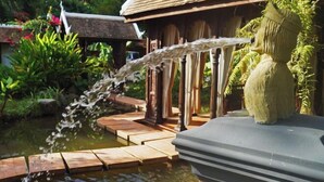 A water feature with a stone pathway leading to a pond, surrounded by lush greenery and a traditional building. - Chateau Orientale (Luang Prabang)