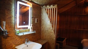 Un baño de cabaña de madera con un lavabo blanco, un espejo y zona de ducha.
