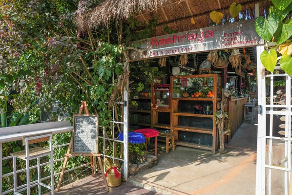 Un pequeño restaurante con techo de paja, un letrero y una exhibición de frutas y verduras.