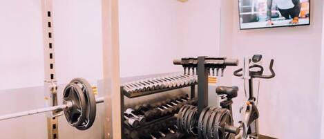 A gym with weightlifting equipment, a bike, and a television on the wall.