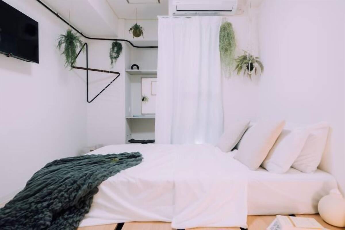 A bedroom with a bed, white curtains, and hanging plants.