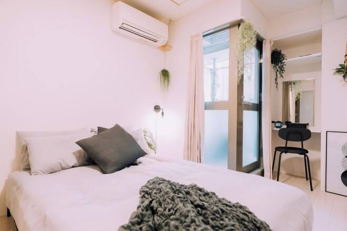 A modern bedroom with a bed, an air conditioning unit, a window, and a chair.