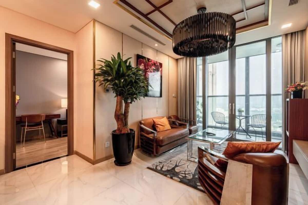 A modern living room with a sofa, a coffee table, a large potted plant, and a chandelier.