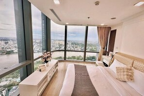 Une chambre spacieuse avec un grand lit, une table de chevet et une vue sur le paysage urbain grâce à de grandes fenêtres.
