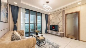 A modern living room with a sofa, a coffee table, a TV, and a large window with curtains. - Condotel Imperial Landmark 81 (Ho Chi Minh City)