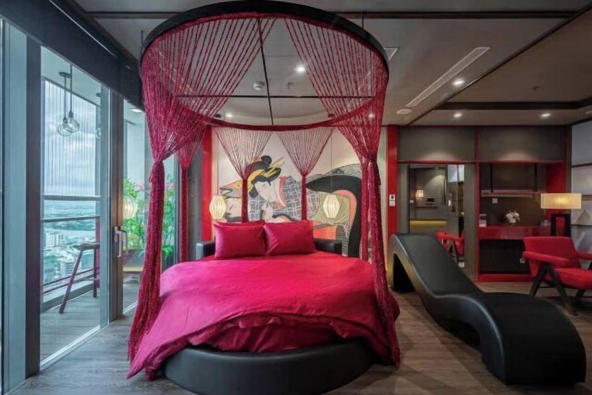 A modern bedroom with a circular bed, a red canopy, and a city view.
