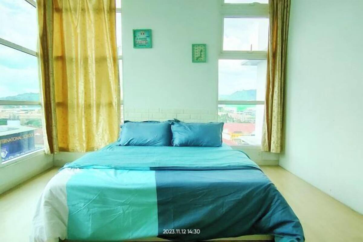A bed in a corner room with a window, curtains, and a view of a cityscape.