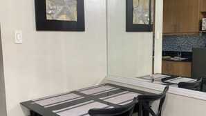 A dining area with a table and chairs, a mirror reflecting the room, and a kitchen area with wooden cabinets and a tiled backsplash. - MOA Shell Residence tower A Kai’STAYCATION (Pasay)