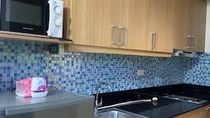 A kitchen with wooden cabinets, a black countertop, a stainless steel sink, and a microwave. - MOA Shell Residence tower A Kai’STAYCATION (Pasay)