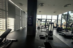 A gym with exercise equipment, large windows, and a view of buildings. - Tropicana 218 With Sea View by LS Staycation (George Town)