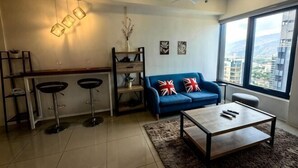 A modern living room with a blue sofa, a coffee table, and a bar area with stools. - Tropicana 218 With Sea View by LS Staycation (George Town)