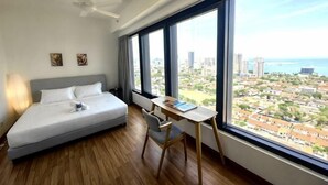 A bedroom with a bed, a desk, and a large window with a city view. - Tropicana 218 With Sea View by LS Staycation (George Town)
