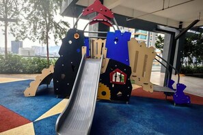 A playground with a slide, climbing structures, and a red and blue playhouse. - Tropicana 218 With Sea View by LS Staycation (George Town)