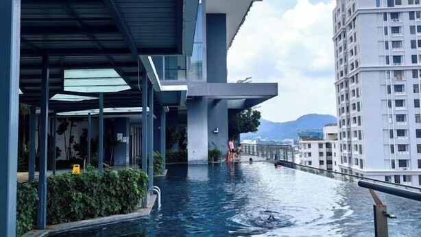 A modern building with a rooftop pool area, surrounded by high-rise buildings and a mountainous backdrop. - Tropicana 218 With Sea View by LS Staycation (George Town)