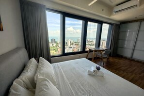 Ein Hotelzimmer mit Bett, kleinem Tisch, Stuhl, großen Fenstern und Stadtblick sowie einem Kleiderschrank.